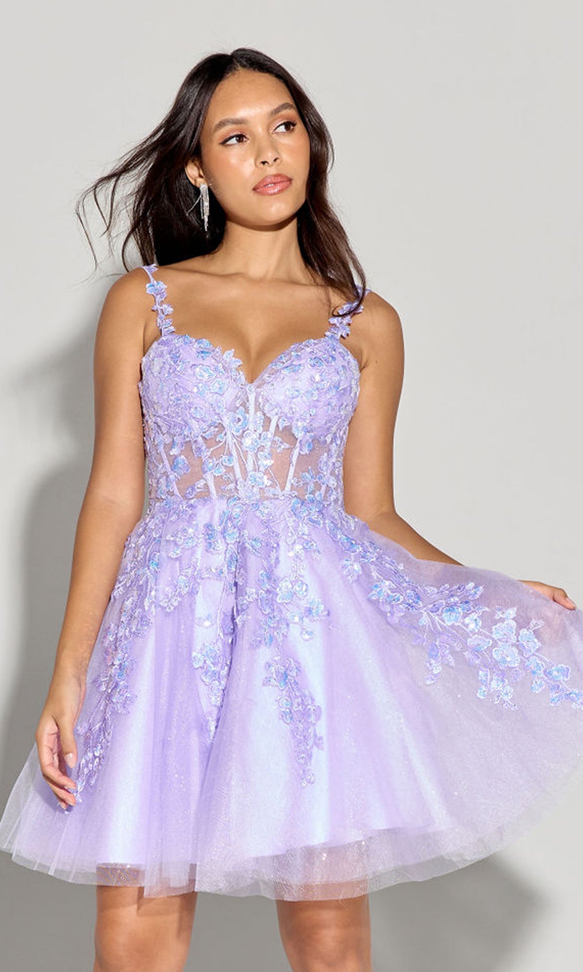 A woman wearing the Eureka EK152 Short Fit-and-Flare Lace Hoco Dress with spaghetti straps and light purple embroidered lace stands against a plain gray background.